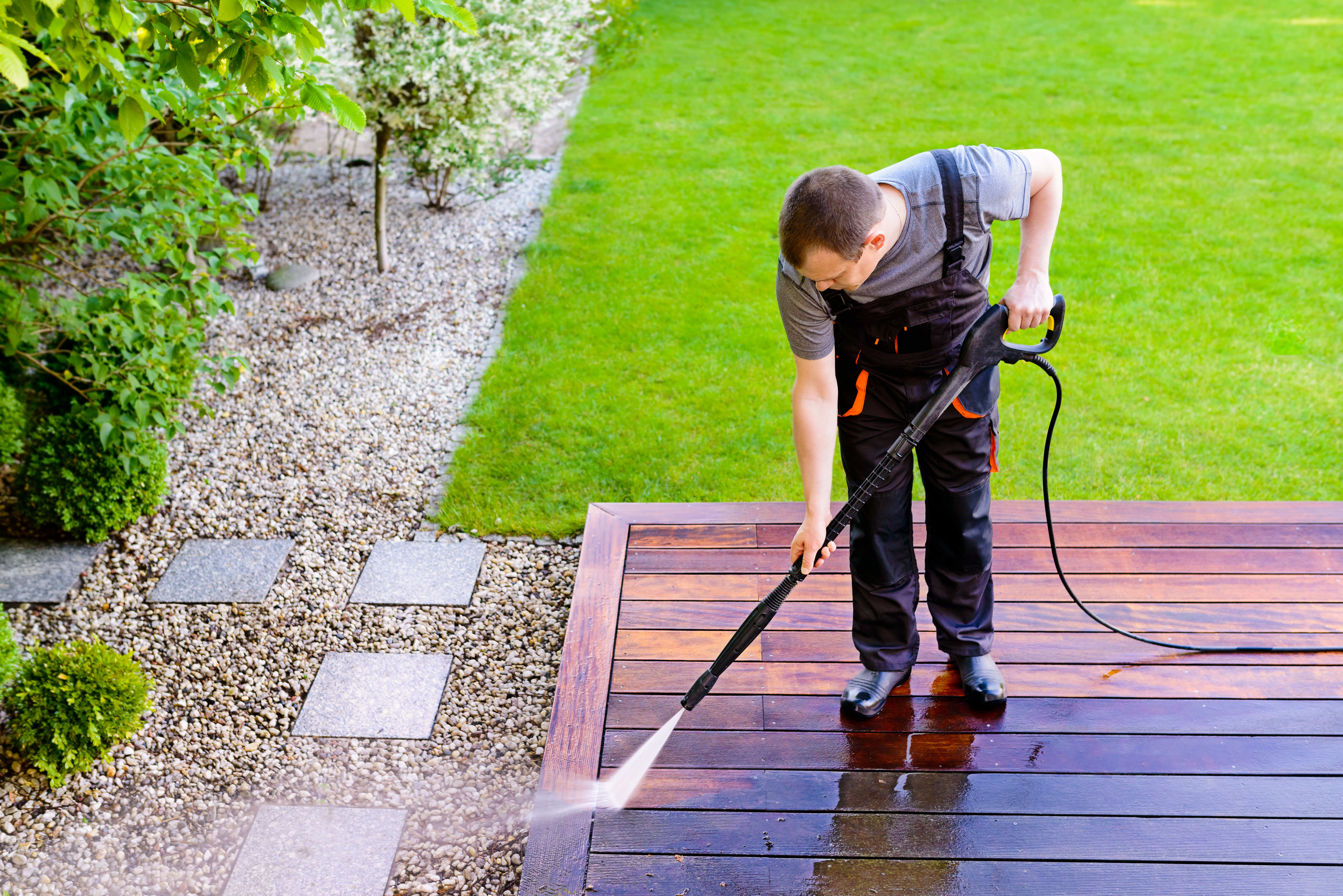 Man using a pressure washer on a wooden patio